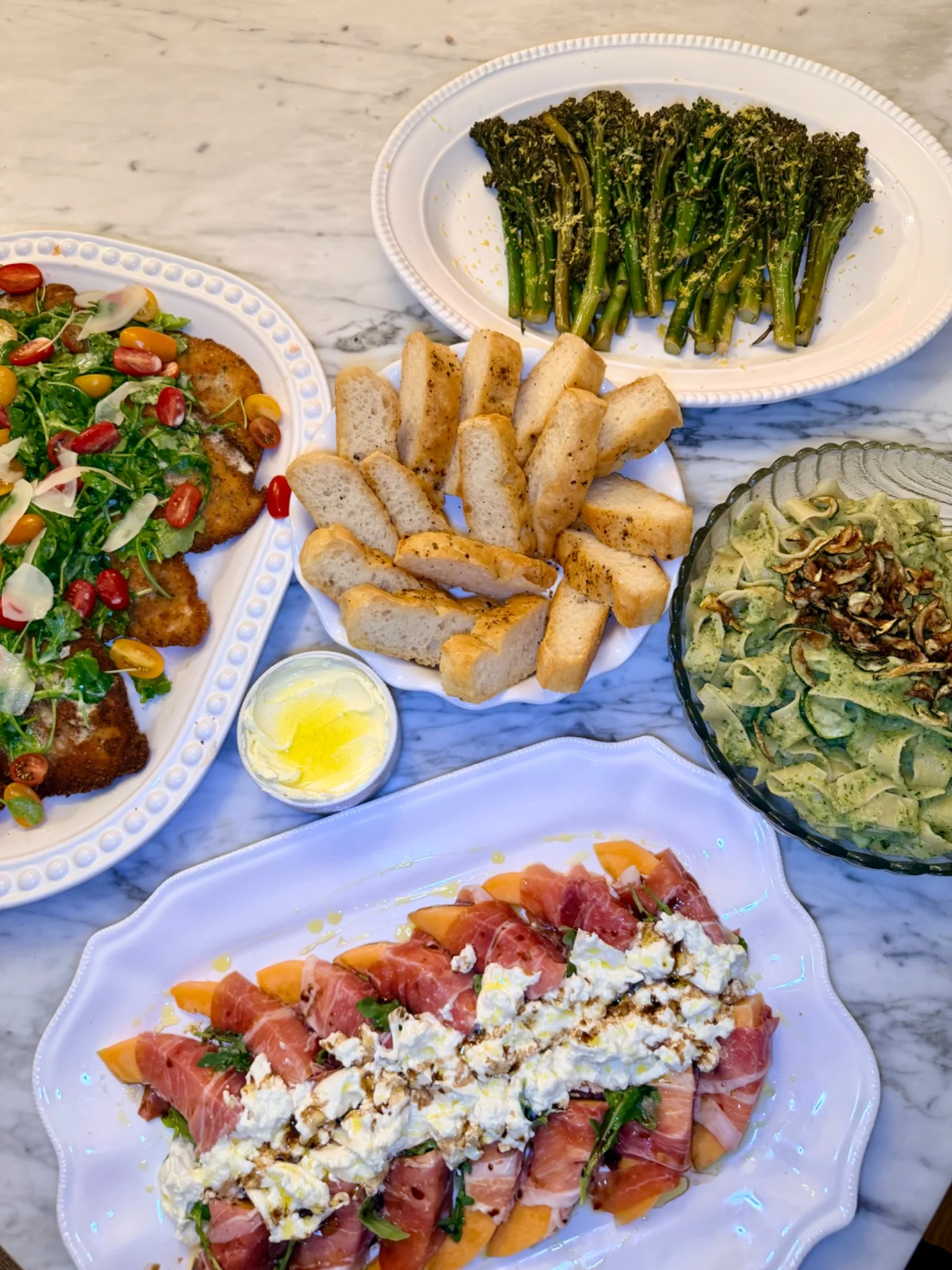 A summer dinner spread with salad, focaccia, broccolini, and green pasta