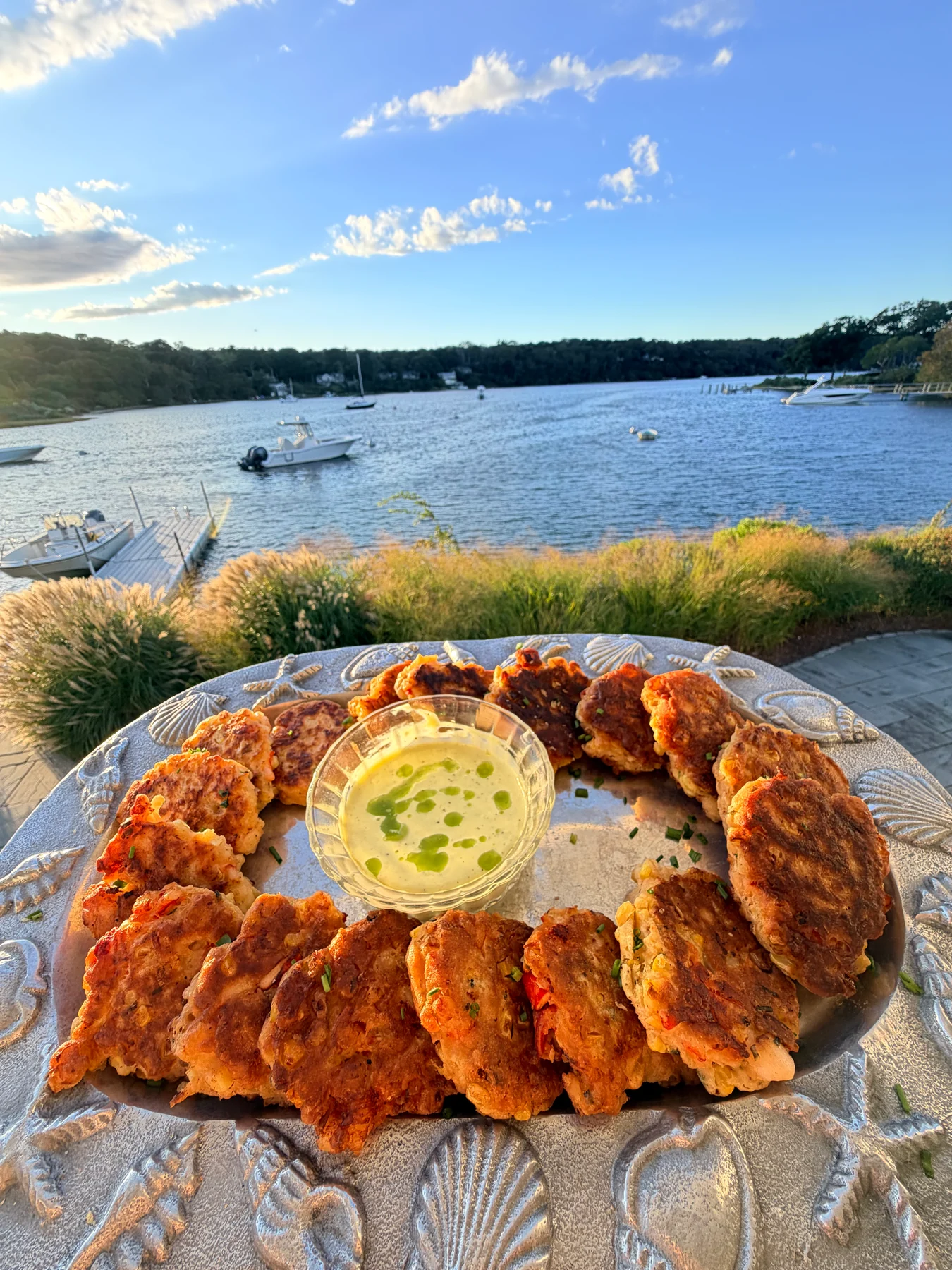 Golden pan-seared appetizers with dipping sauce on a shell-patterned platter overlooking a harbor