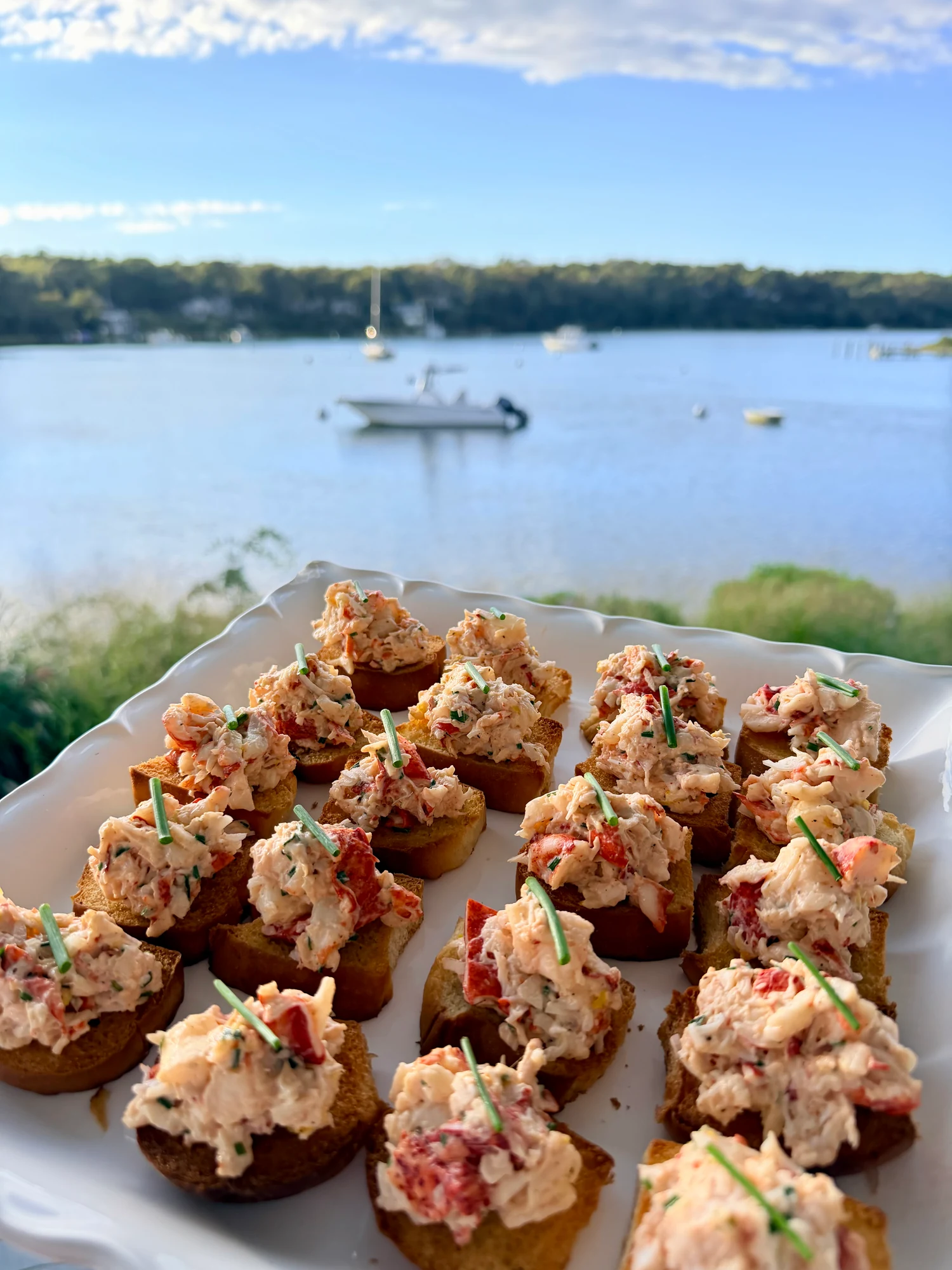 Lobster crostini on a white platter overlooking a coastal harbor